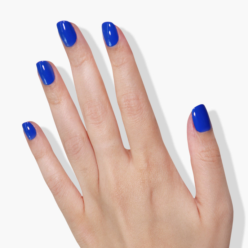 A hand with neatly manicured nails painted in LONDONTOWN's Iconic, a vibrant electric blue nail polish that won the 2019 Allure Best of Beauty Award, against a white background.